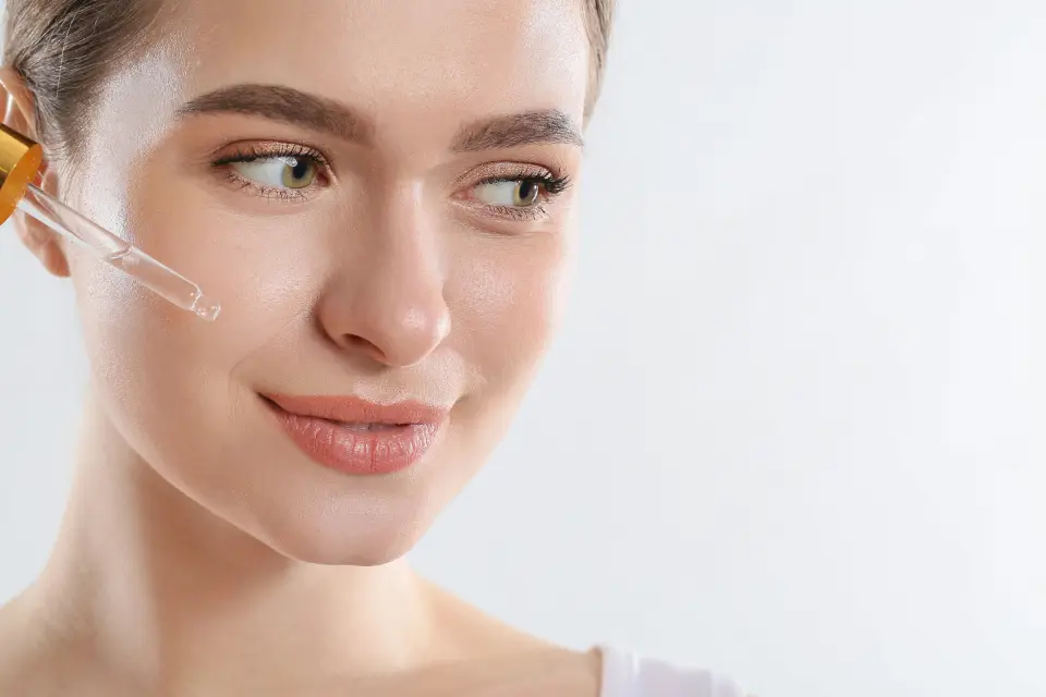 Mulher aplicando sérum facial, com a pele uniforme e hidratada