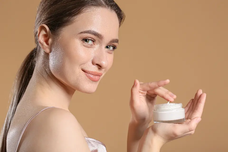 Mulher sorrindo e segurando um pote de creme, em fundo bege