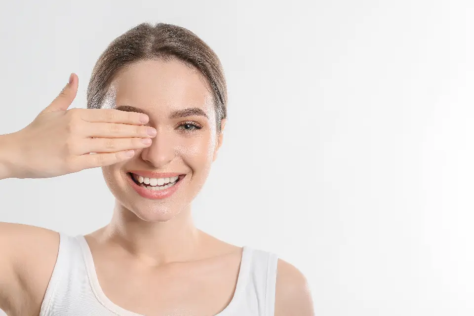 Mulher sorridente cobrindo um dos olhos com a mão, sobre fundo branco