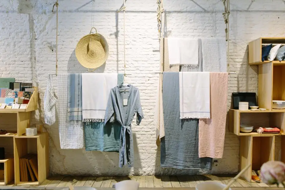 Interior da boutique com paredes de tijolo branco, peças em linho penduradas e chapéu de palha