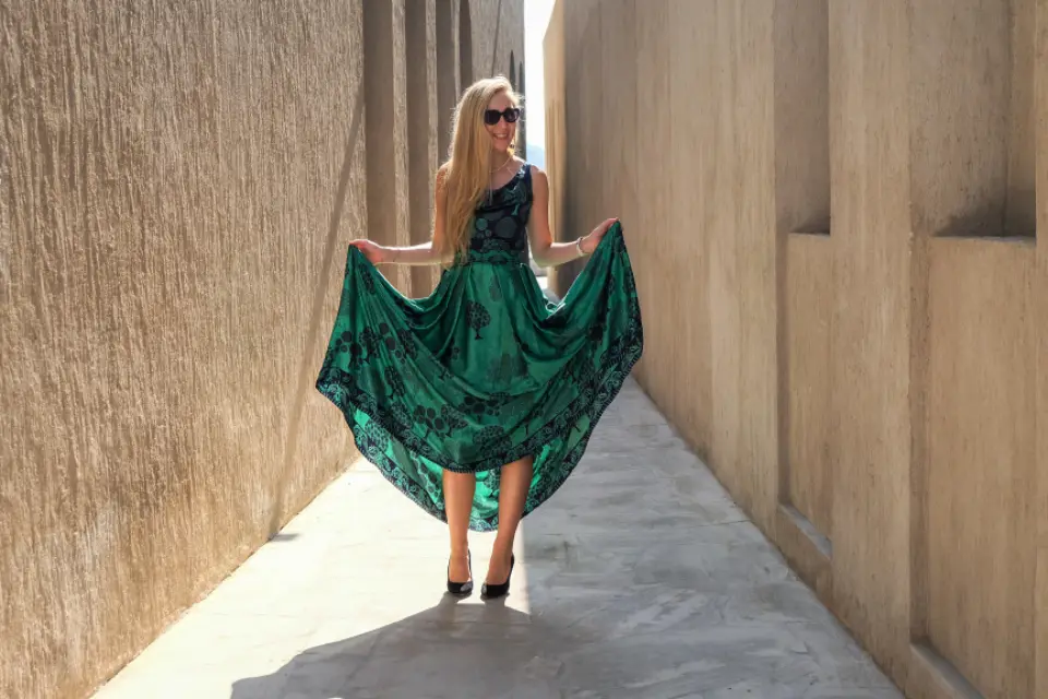 Mulher caminhando em uma viela com vestido verde esmeralda, segurando a saia rodada