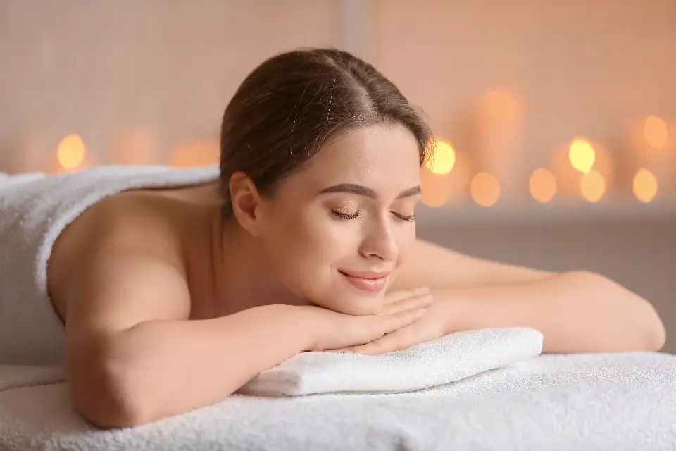 Mulher de olhos fechados relaxando sobre a maca de massagem, com velas acesas ao fundo