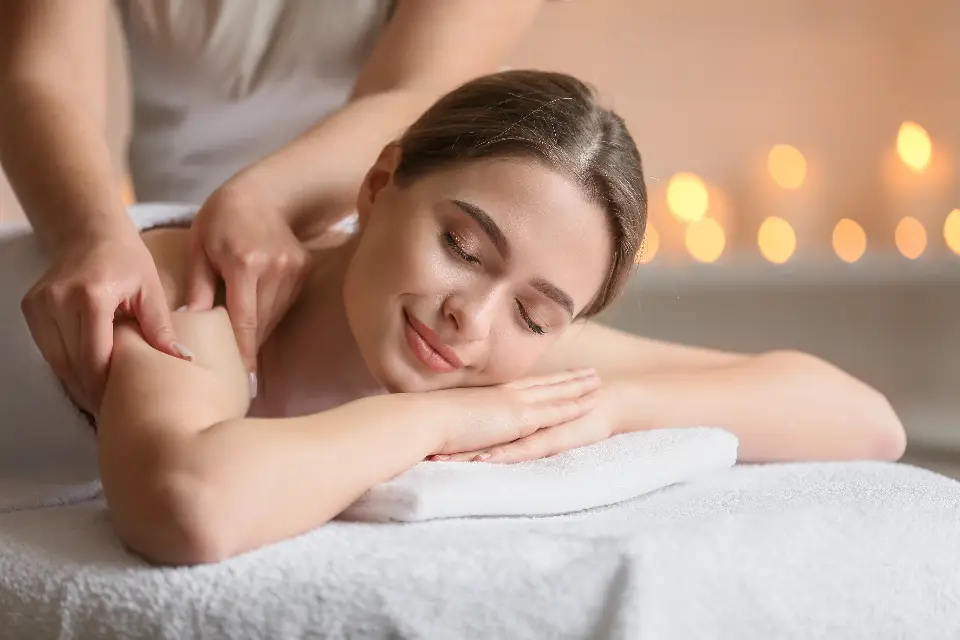 Mulher sorrindo de olhos fechados enquanto recebe massagem nos ombros