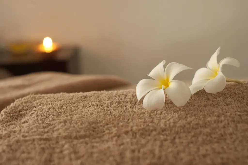 Flores brancas sobre toalha felpuda bege, com uma vela acesa ao fundo
