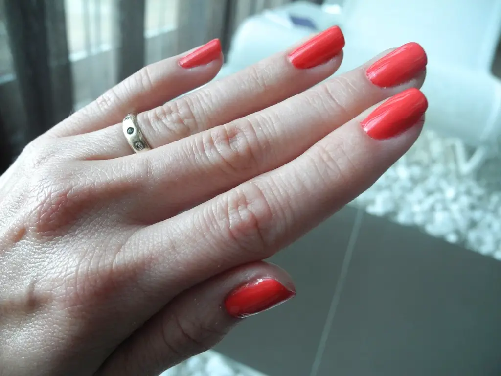 Close de mão com unhas curtas esmaltadas em vermelho coral e anel dourado