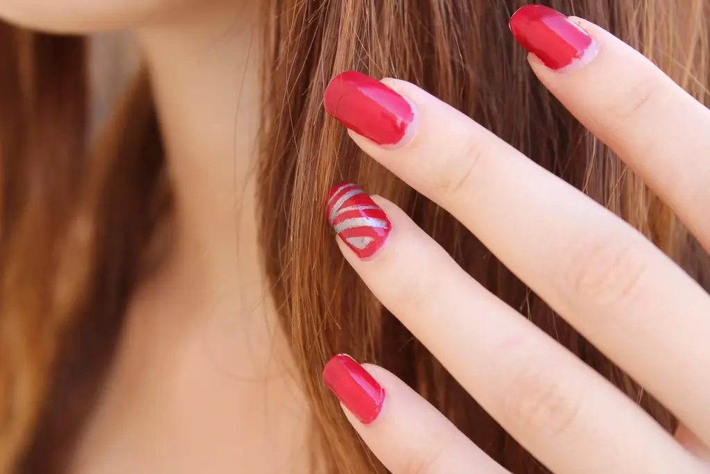 Unhas vermelhas tocando o cabelo, com nail art de listras prateadas em um dos dedos