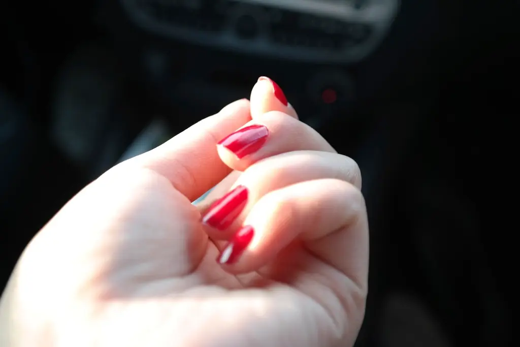 Mão com unhas esmaltadas em gel vermelho cereja, iluminada sobre fundo escuro
