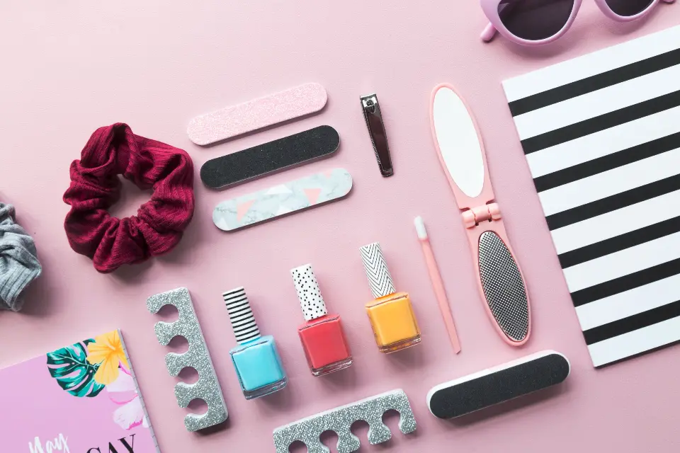 Acessórios de manicure sobre fundo rosa: lixas, alicate, esmaltes coloridos, separadores de dedos e lixa para os pés
